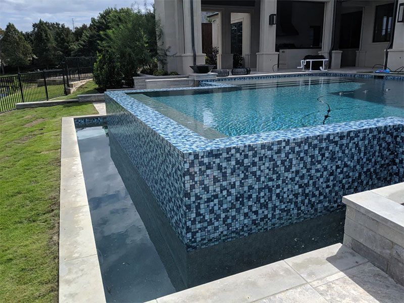 A large swimming pool with blue tiles in front of a house.