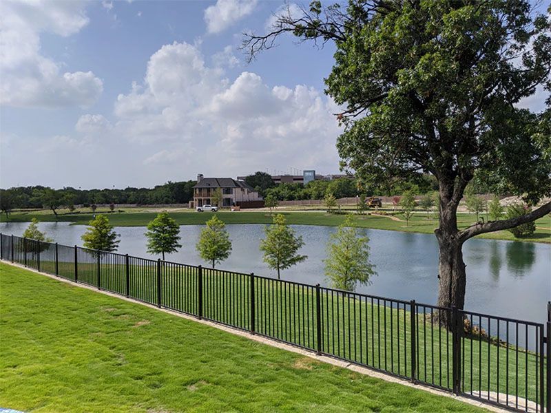 A fence surrounds a lake with trees and a house in the background.