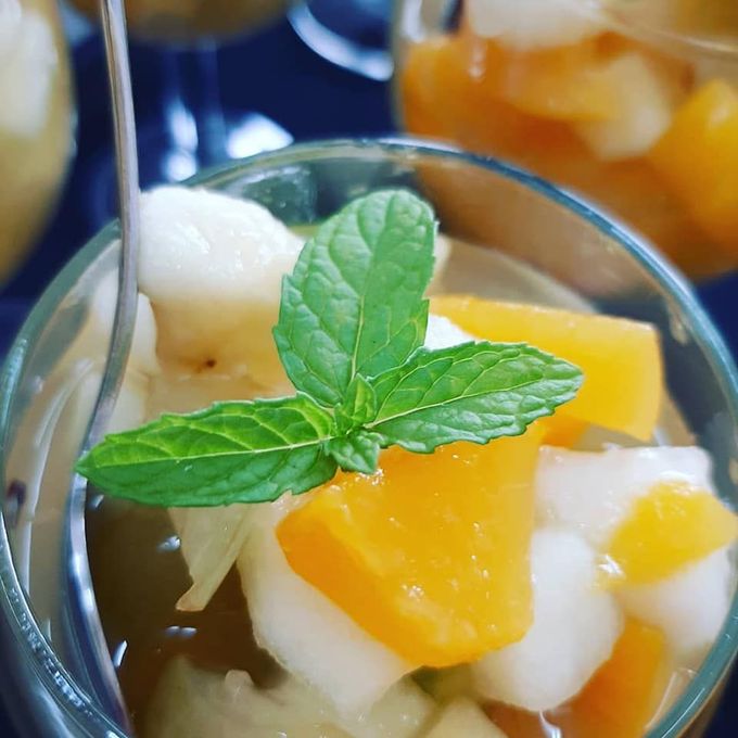 Macedonia di frutta con guarnizione di menta in una ciotola di vetro.