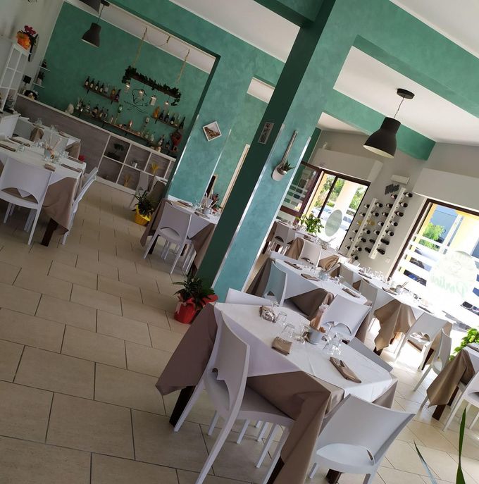 Luminoso interno del caffè con tavoli e sedie bianchi, colonne color verde acqua e grandi finestre che lasciano entrare la luce naturale.
