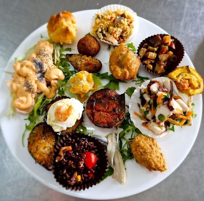 Assortimento di antipasti salati su un piatto bianco, tra cui pasticcini, frittelle, insalata e salse.