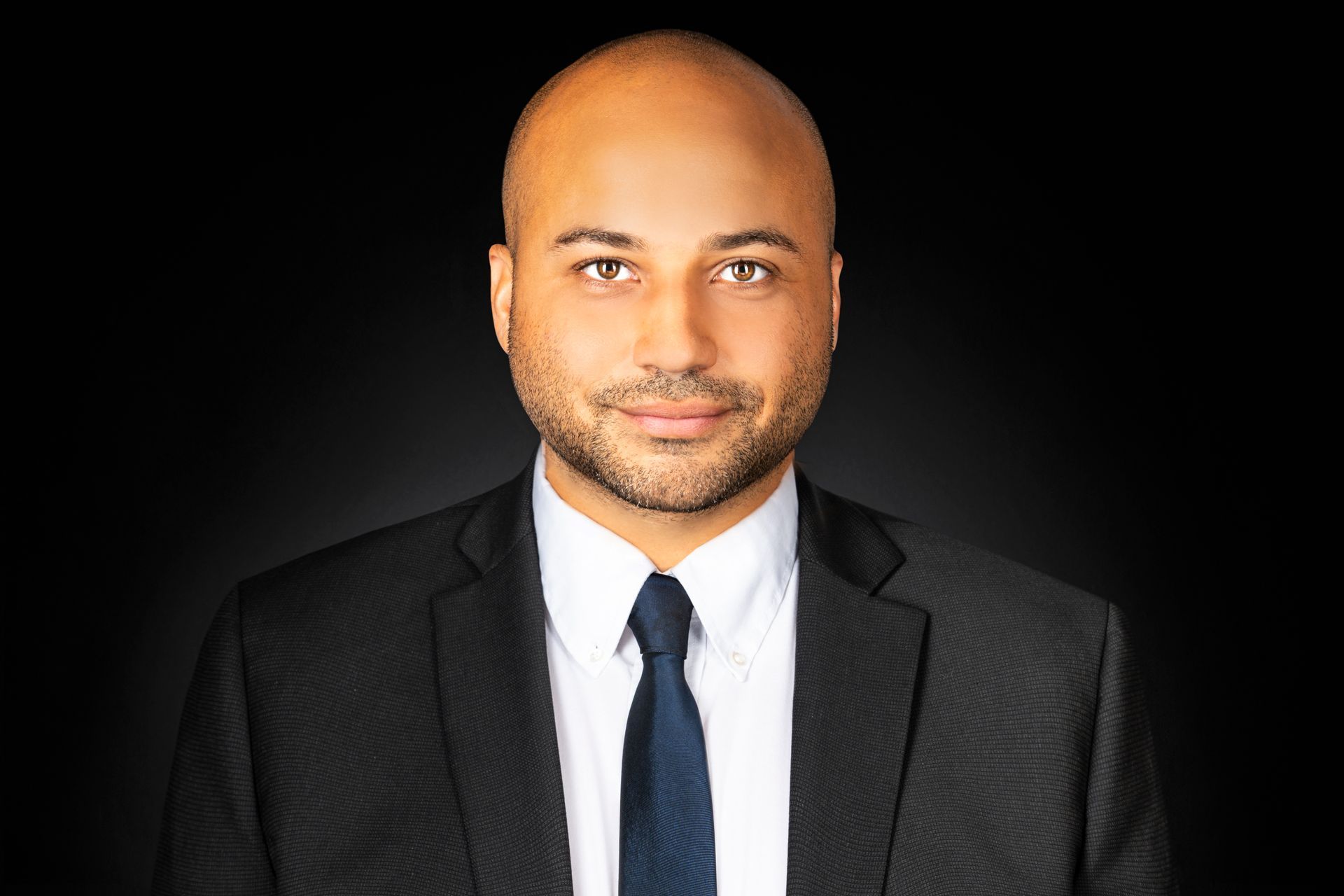 A bald man in a suit and tie is looking at the camera.