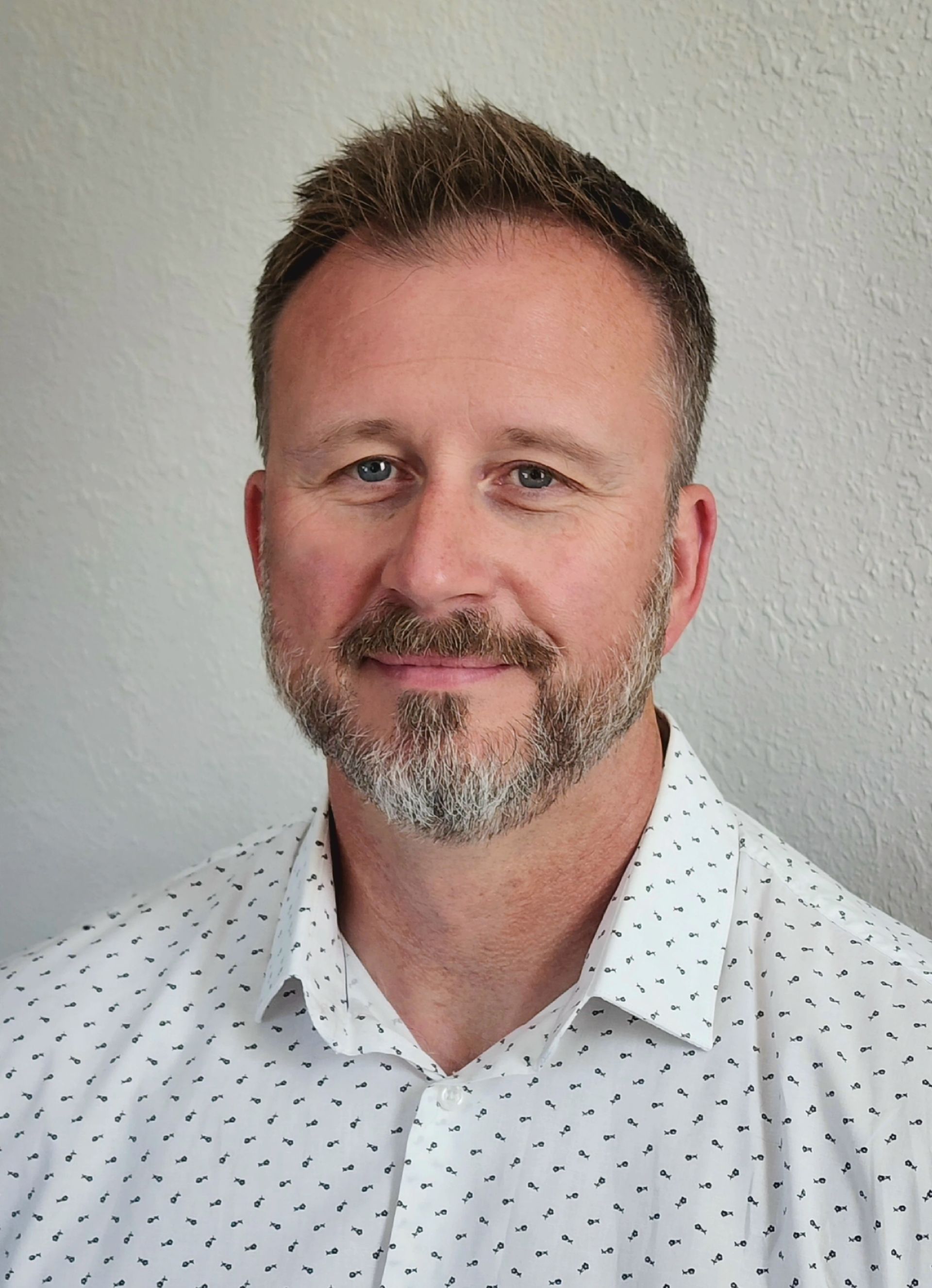A man with a beard is wearing a white shirt and smiling for the camera.