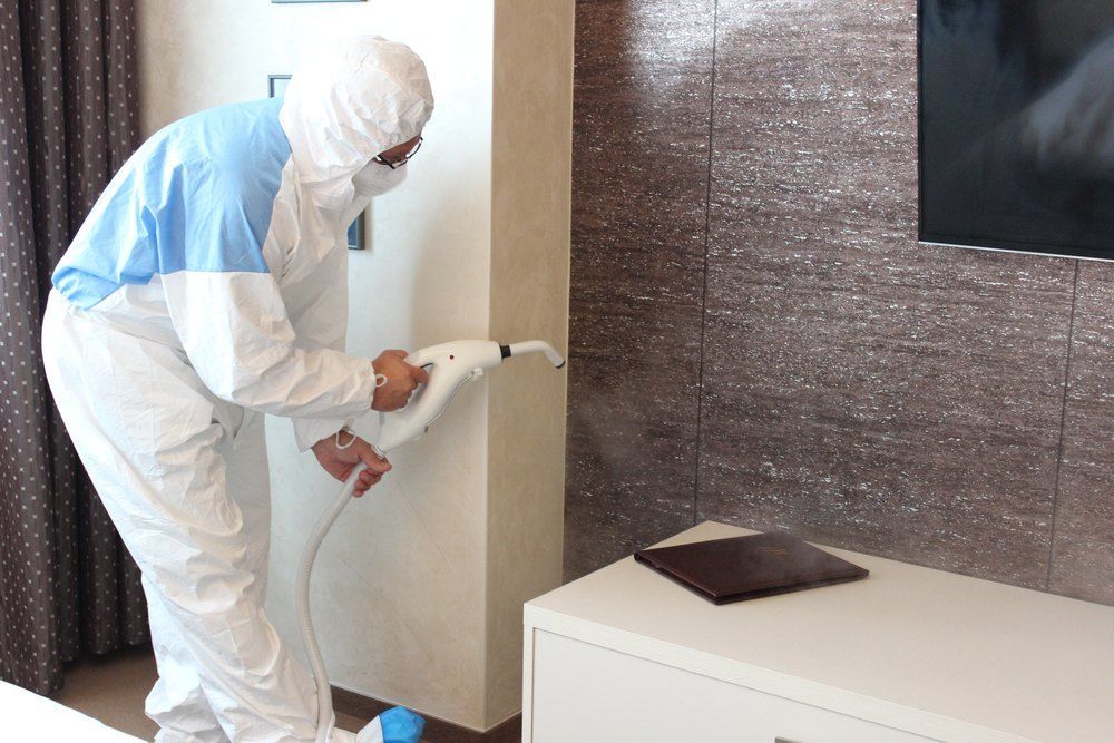Person in Hazmat Suit Sanitizing a Room With a Sprayer — Optimum Pest Services In Atherton, QLD