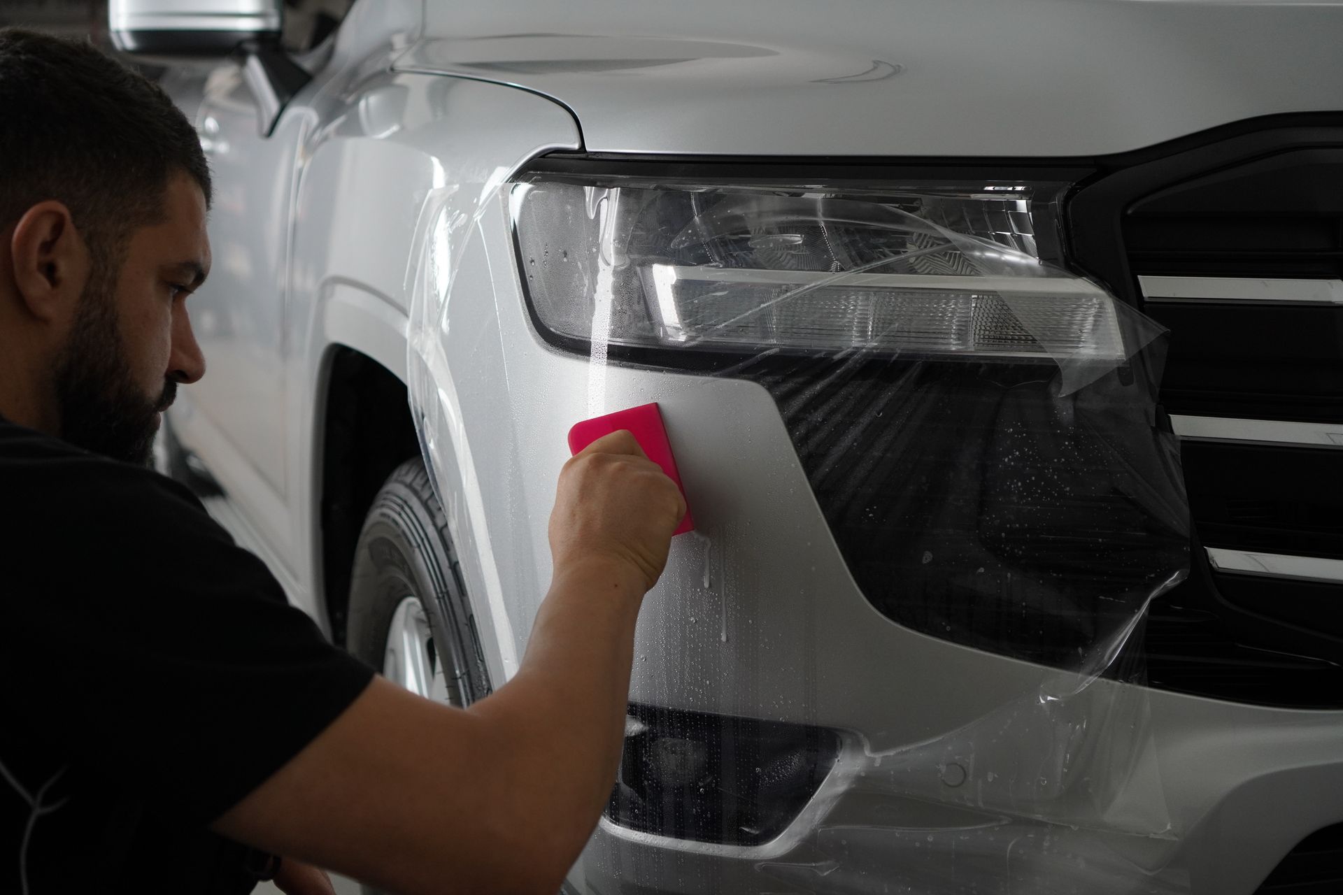 A man is applying a protective film to the front of a silver car.