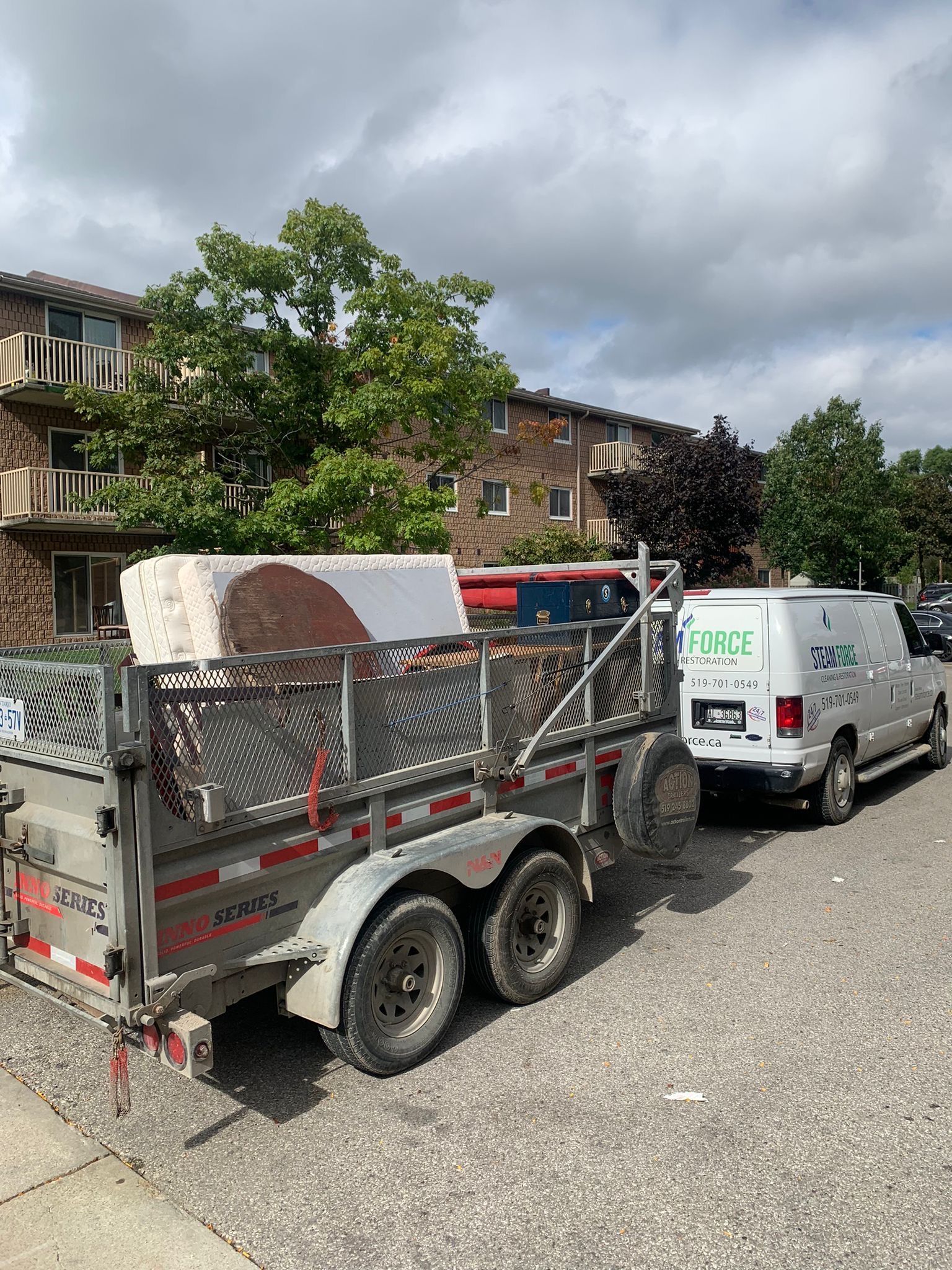 A trailer is being pulled by a white van on a street.