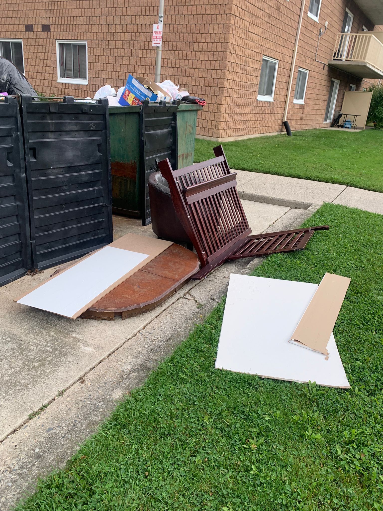 A couch is laying on the sidewalk next to a trash can.