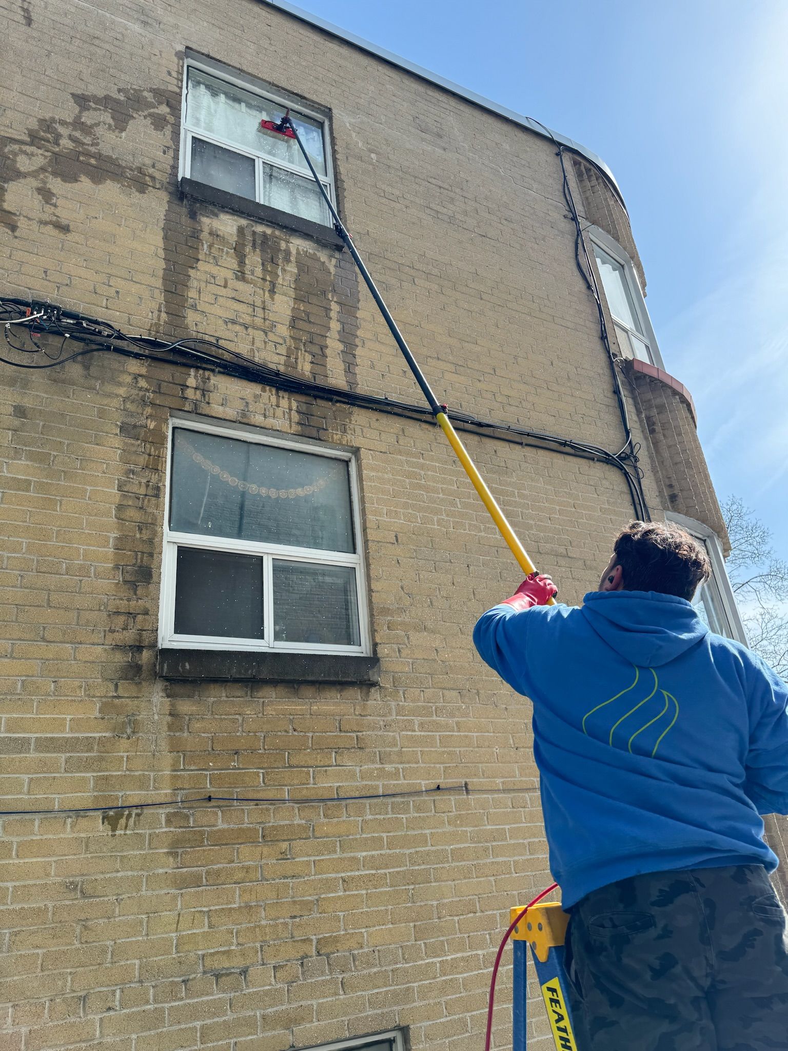 A man is cleaning a window on the side of a brick building.