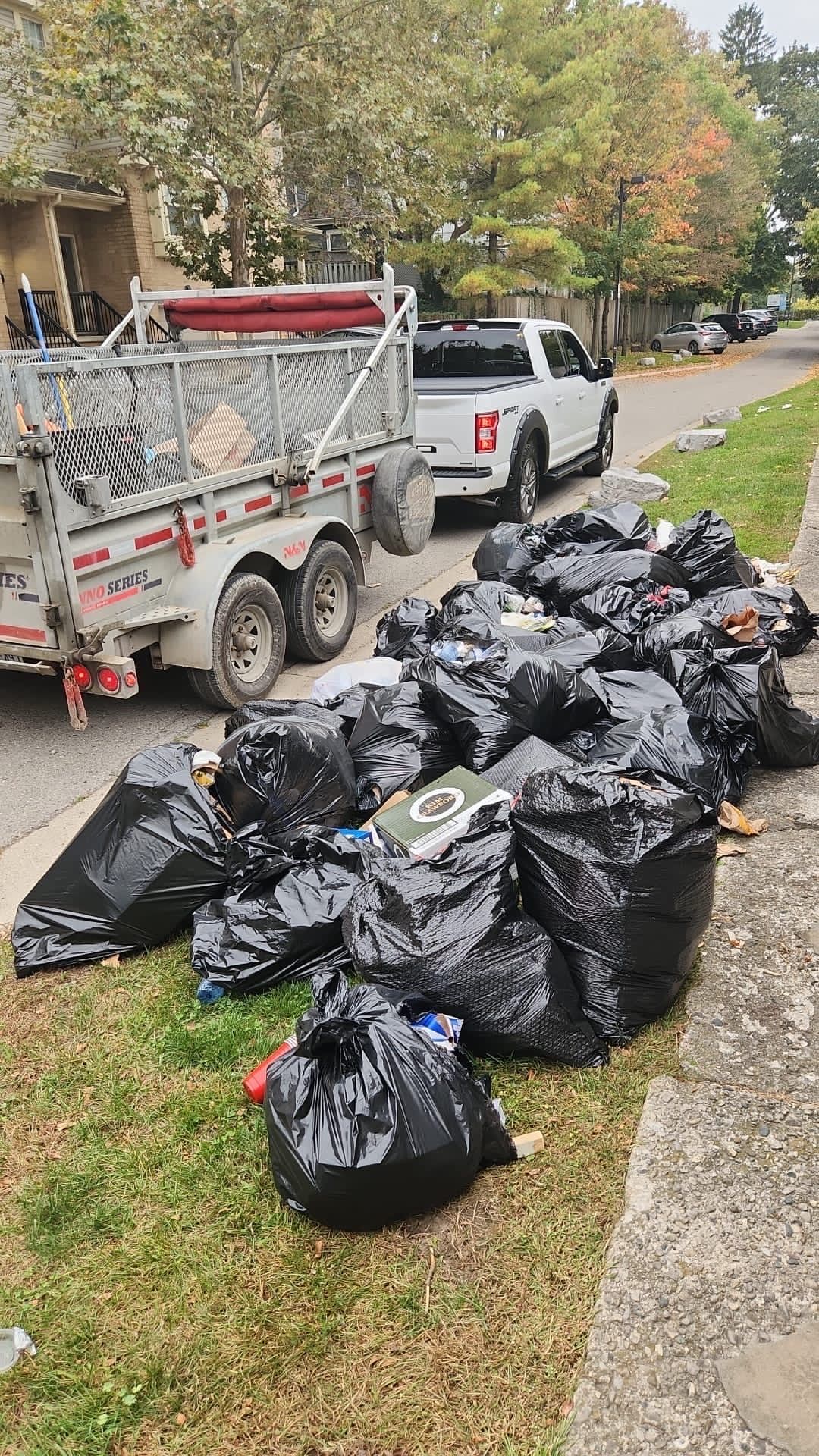 A truck is parked next to a pile of trash bags on the side of the road.