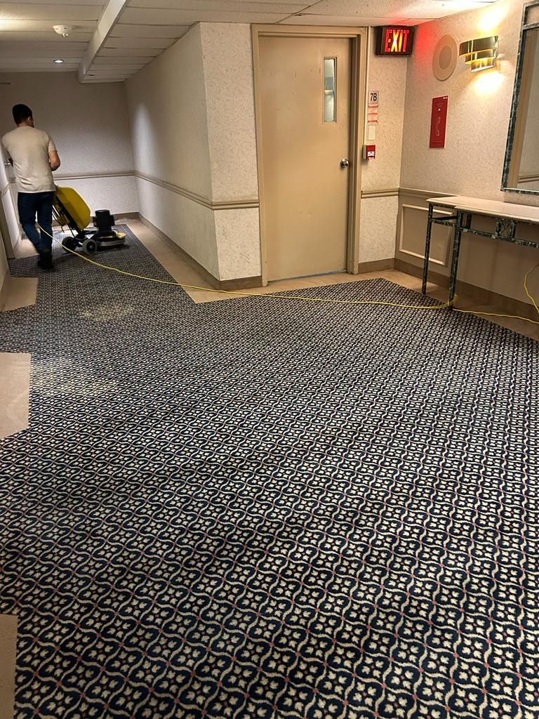 A man is walking down a hallway with a lot of carpet on the floor.