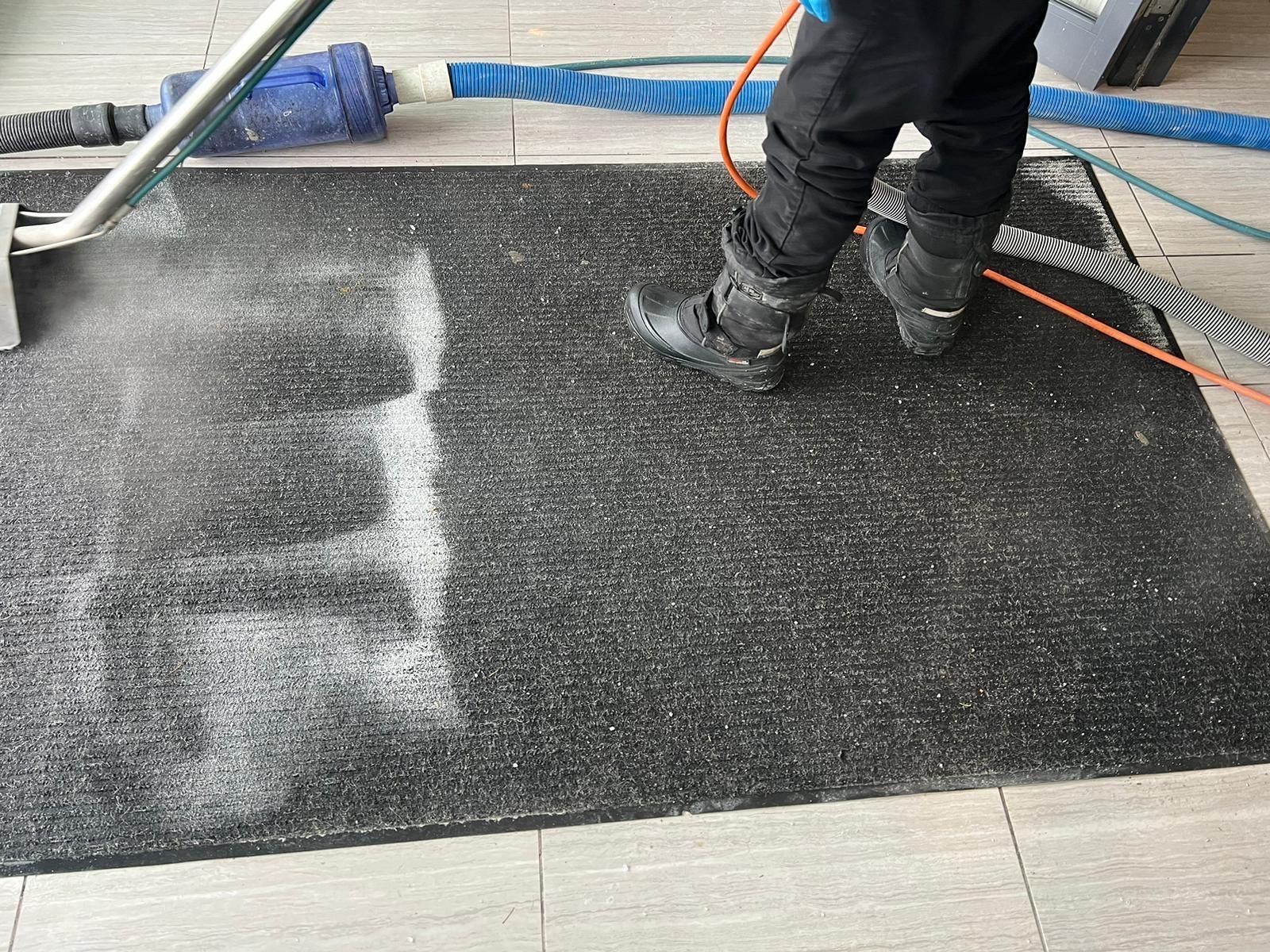 A person is cleaning a door mat with a vacuum cleaner.