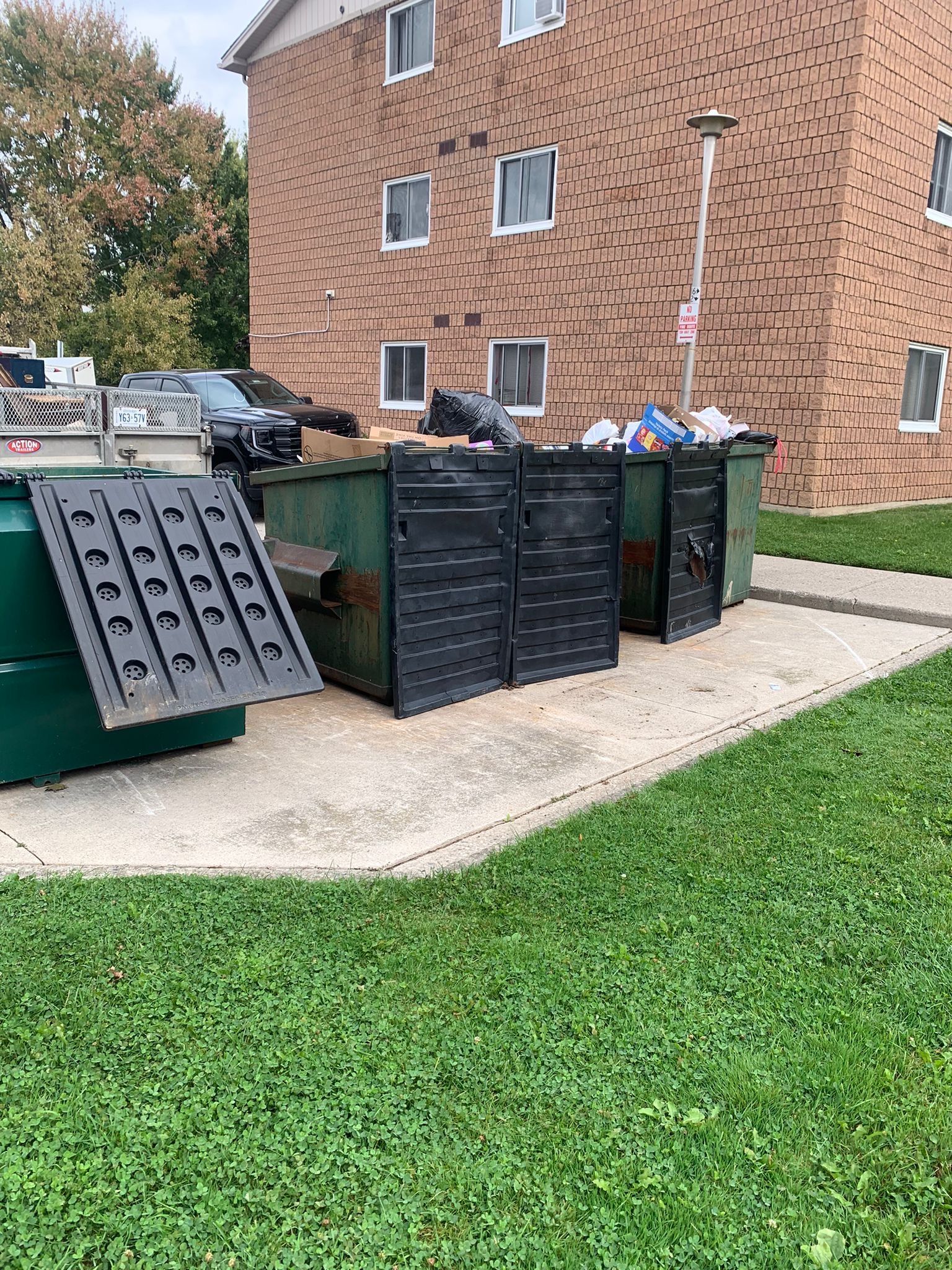 A row of dumpsters are sitting in front of a brick building.