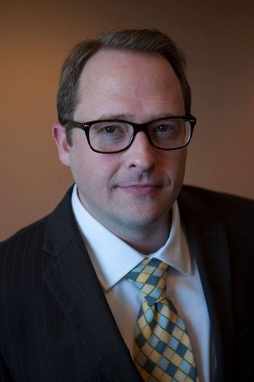 A man in a suit and white shirt is smiling for the camera.
