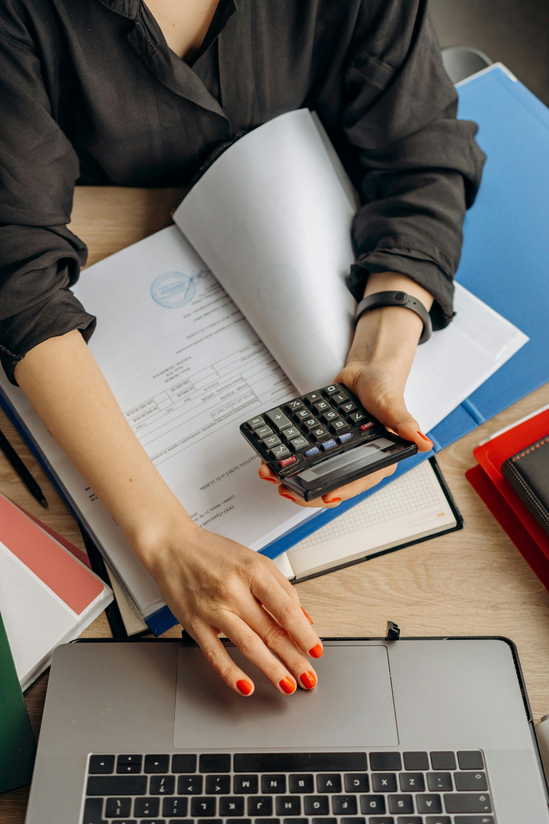 A woman is sitting at a desk using a calculator.