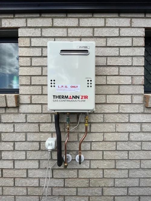 A White Thermann Continuous Flow Gas Water Heater Mounted on a Brick — Mates Plumbing and Gas in Lammermoor, QLD