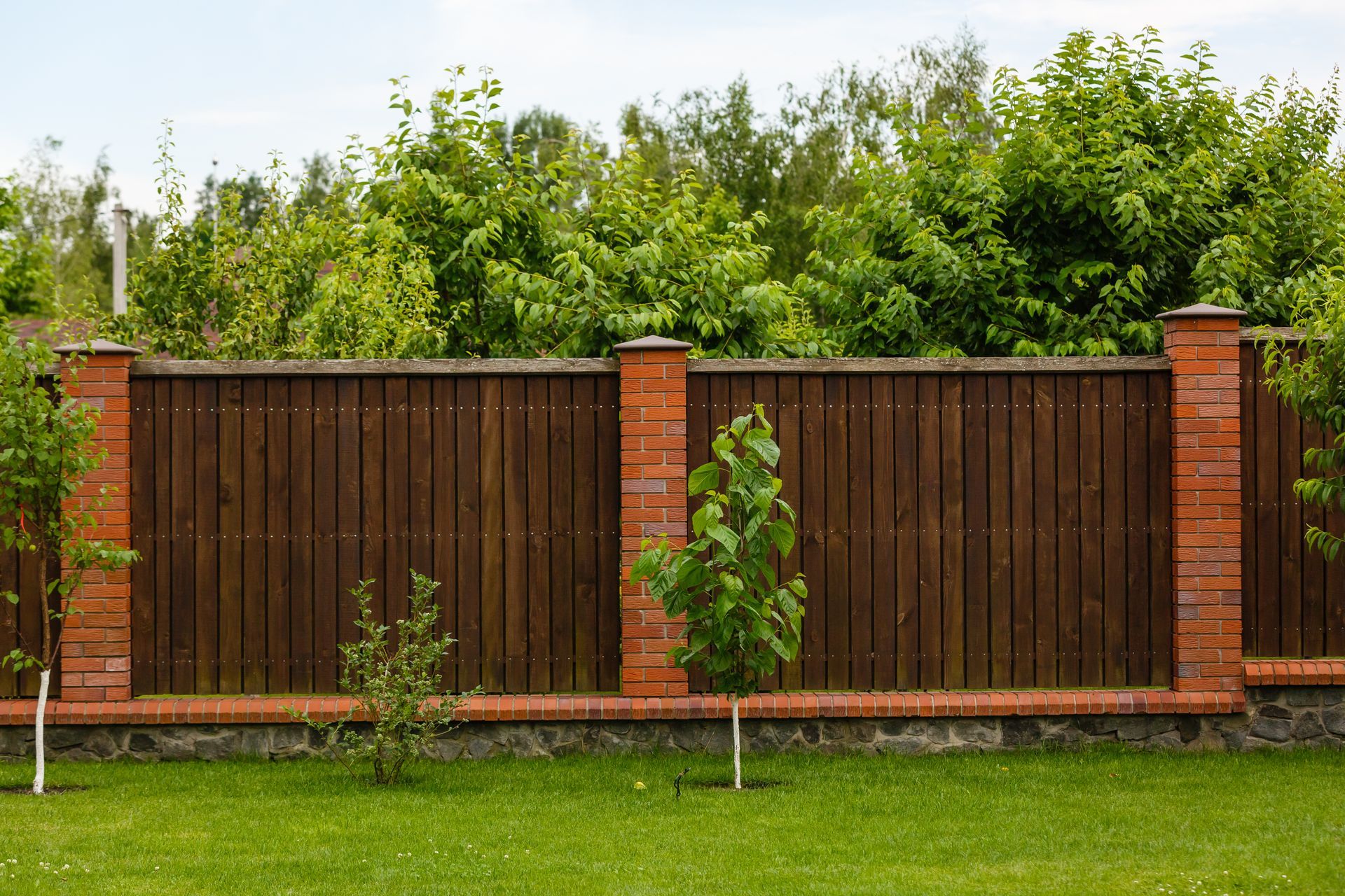 a wooden fence is surrounded by brick pillars and trees