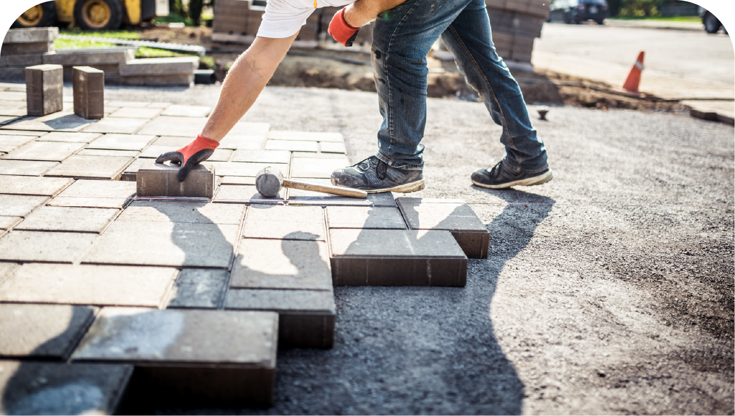 A man is laying bricks on a sidewalk.