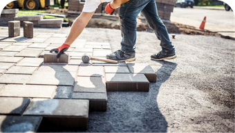 A man is laying bricks on a sidewalk.