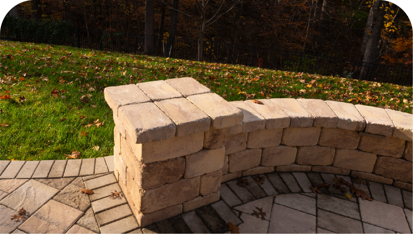 A brick wall surrounds a patio with trees in the background