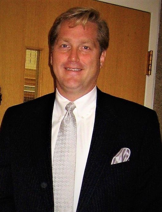 A man in a suit and tie stands in front of a door