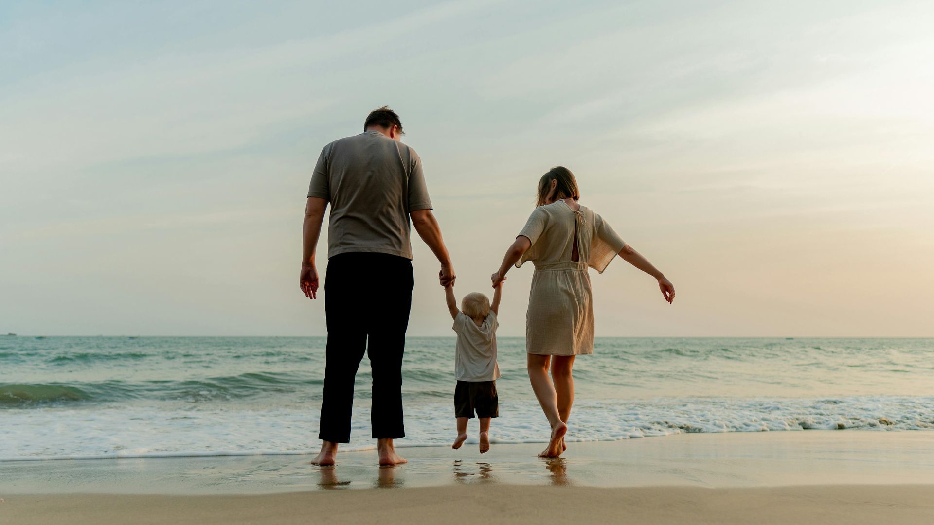 A family is walking on the beach holding hands.