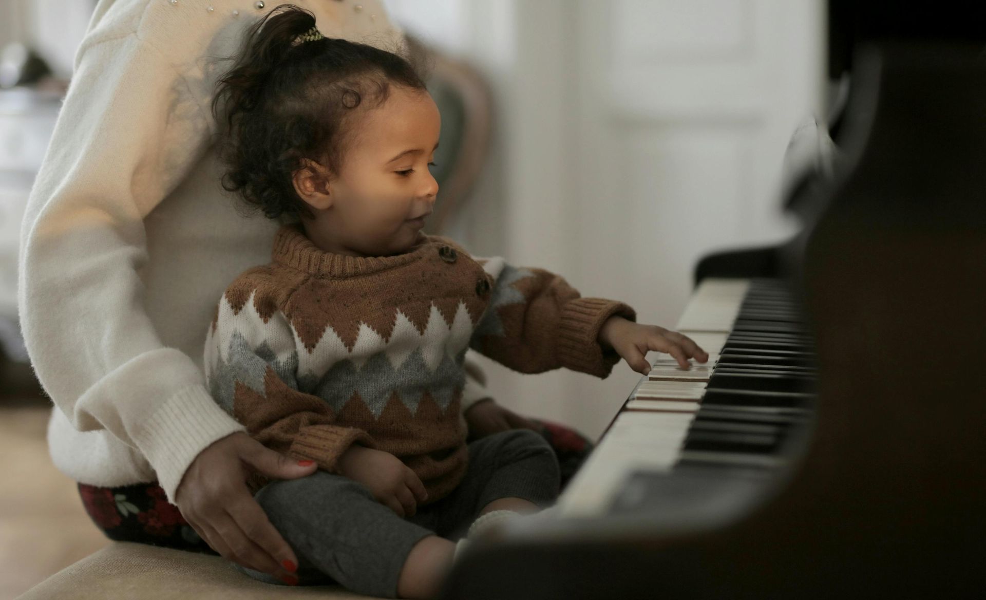 A baby is sitting on a woman 's lap playing a piano.