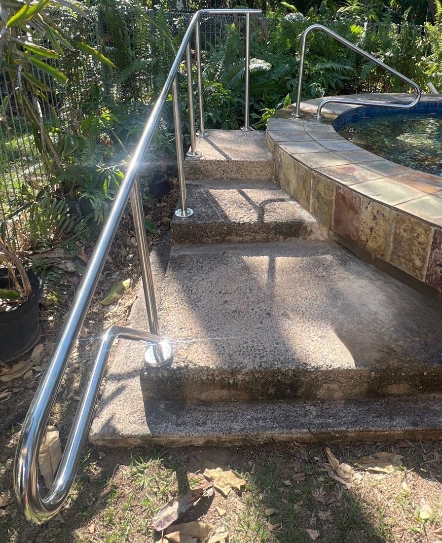 Concrete steps with a stainless steel handrail leading to a pool 