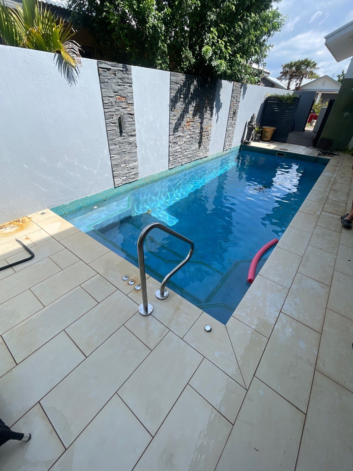 Small rectangular pool with blue water. Cream-colored stone patio. Decorative wall with gray stone inserts  — Friendly Pool & Spa Care in Coconut Grove, NT 
