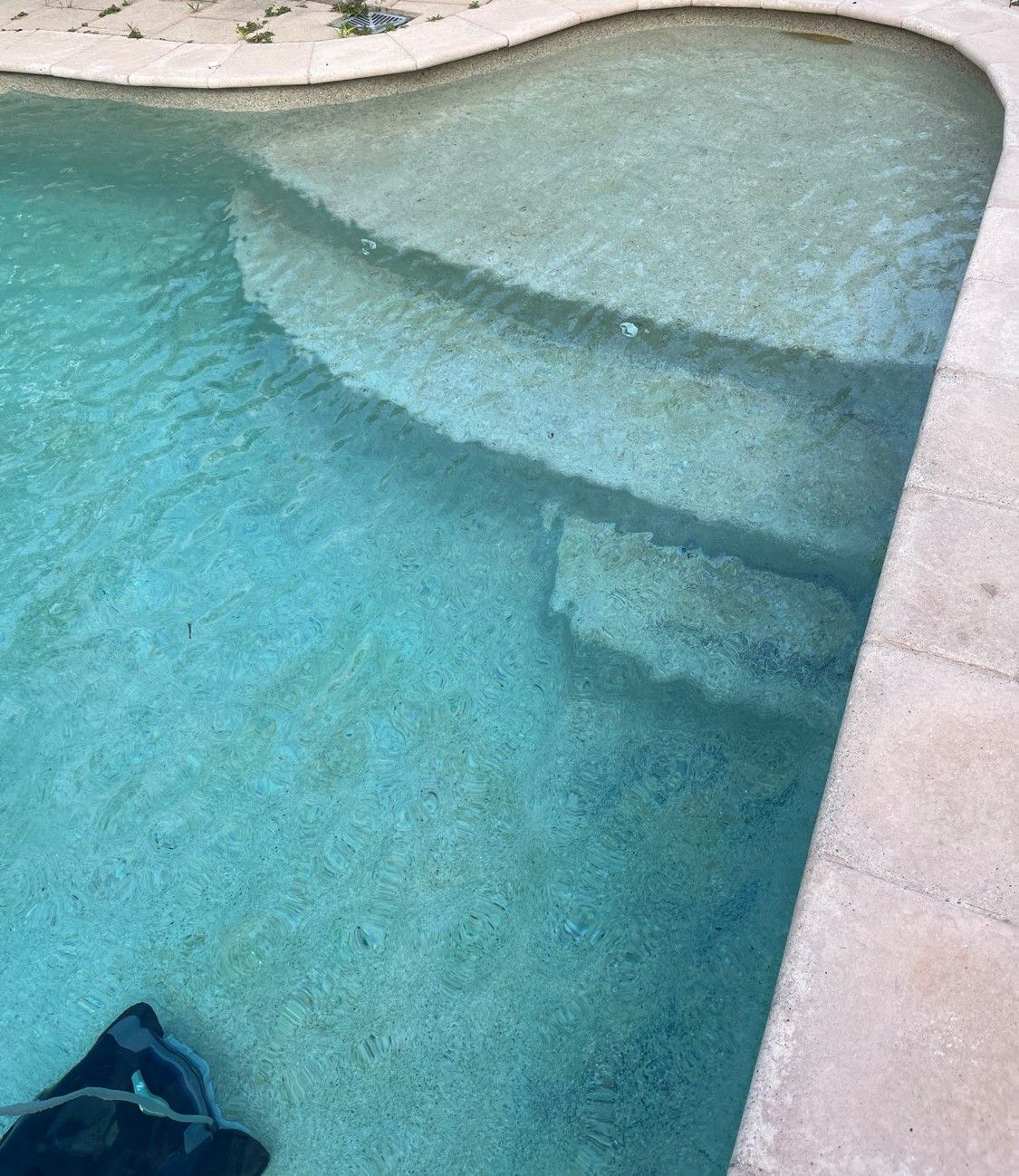Light blue water fills a swimming pool with tiered steps leading into the shallow end, bordered by beige stone coping  — Friendly Pool & Spa Care in Coconut Grove, NT 