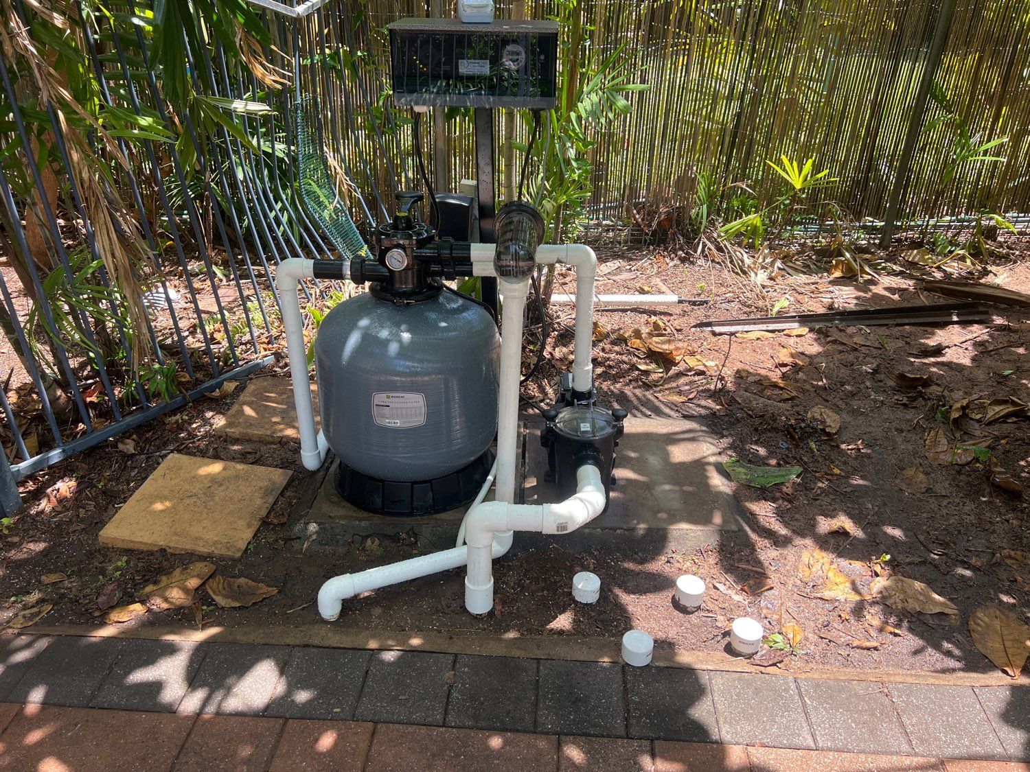 Pool filter system in a backyard, with grey tank, white pipes, and a black pump  — Friendly Pool & Spa Care in Coconut Grove, NT 
