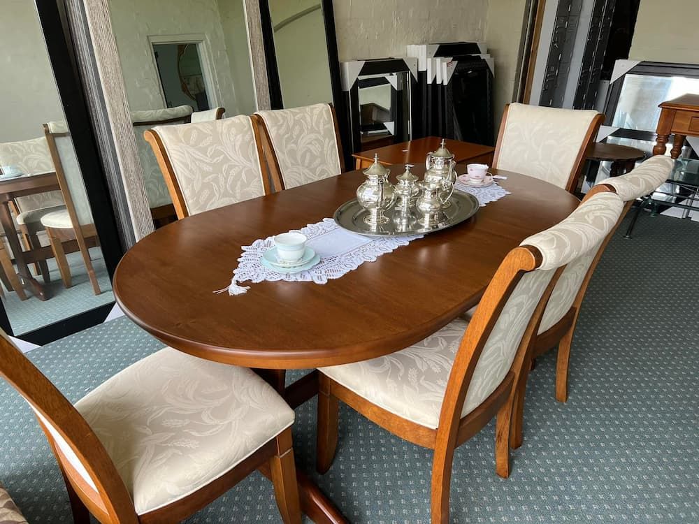 A Wooden Oval Dining Table With Six Cream-coloured Upholstered Chairs — Clancy's Office & Emporium in Taree, NSW