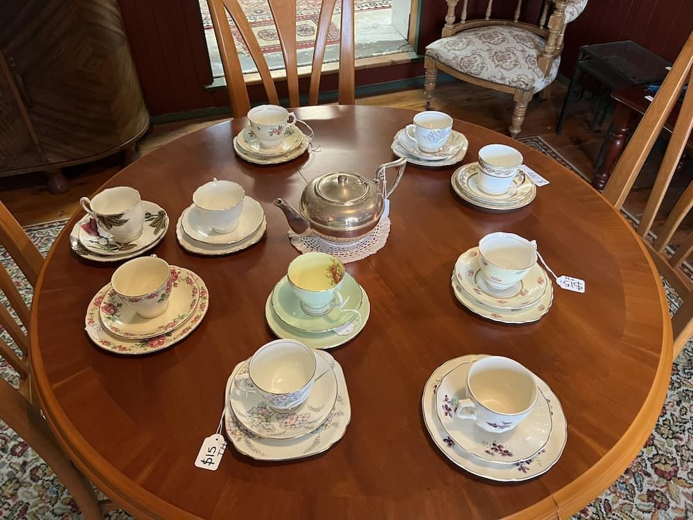 A Round Wooden Table Set for Tea With Cups, Saucers, and a Silver Teapot — Clancy's Office & Emporium in Taree, NSW