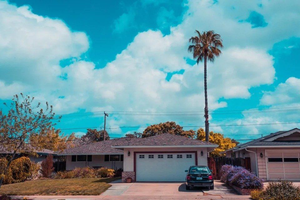 A house with a car parked in front of it and a palm tree.