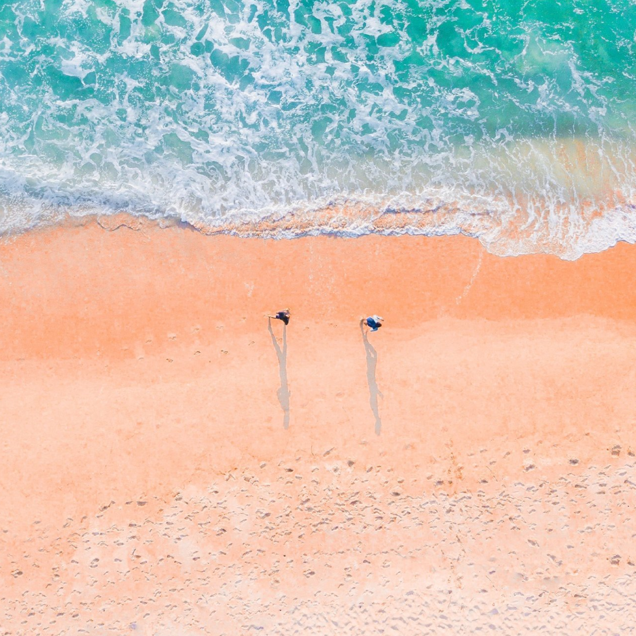 An aerial view of two people standing on a beach with umbrellas.