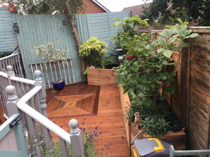 A garden with a wooden deck and a blue fence