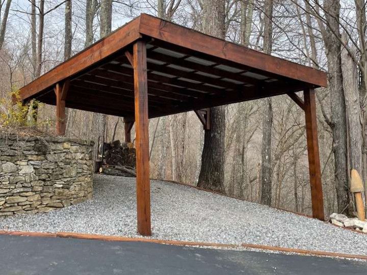 A wooden gazebo is sitting on top of a gravel driveway in the woods .