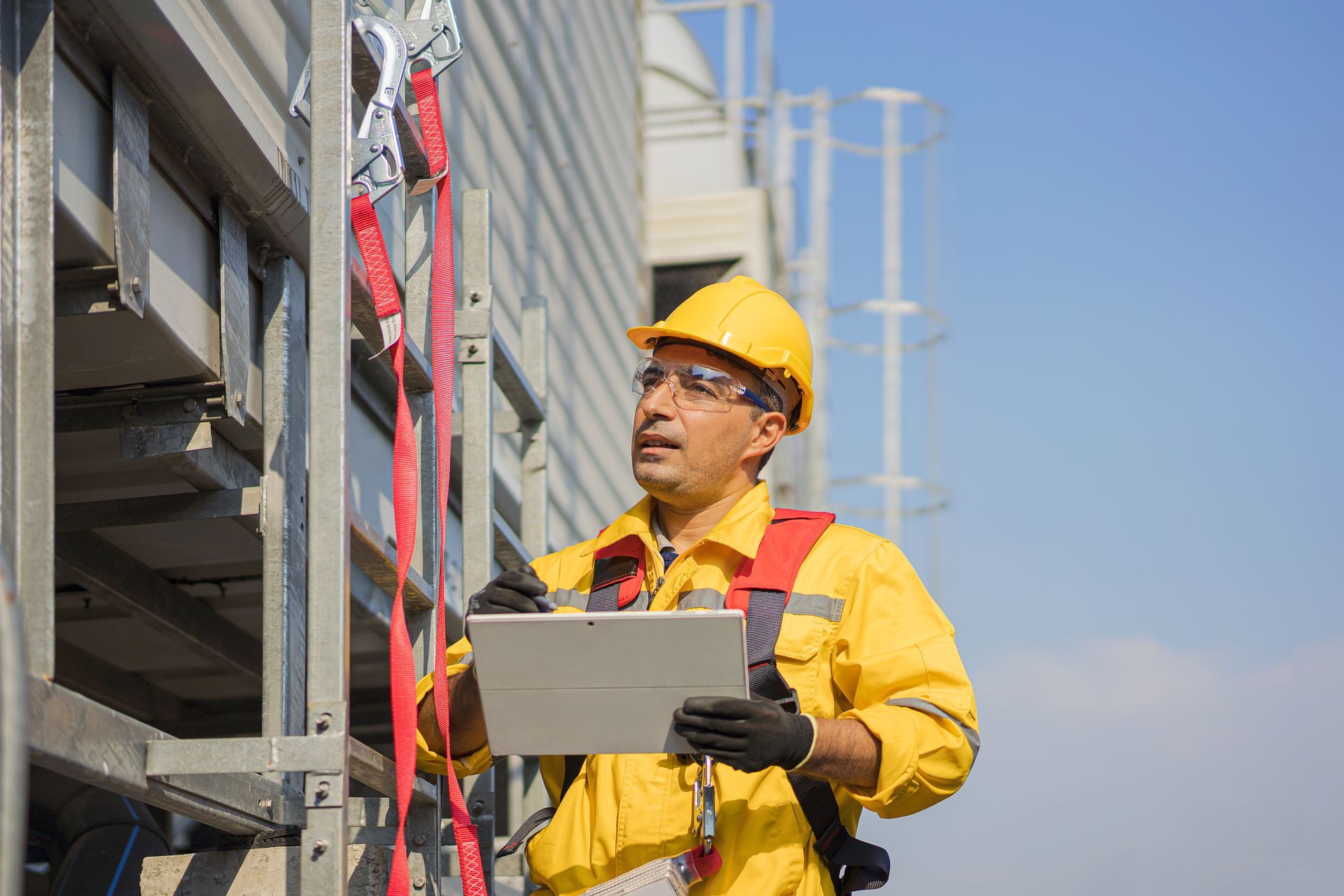 A construction wearing safety harness and using digital tablet.