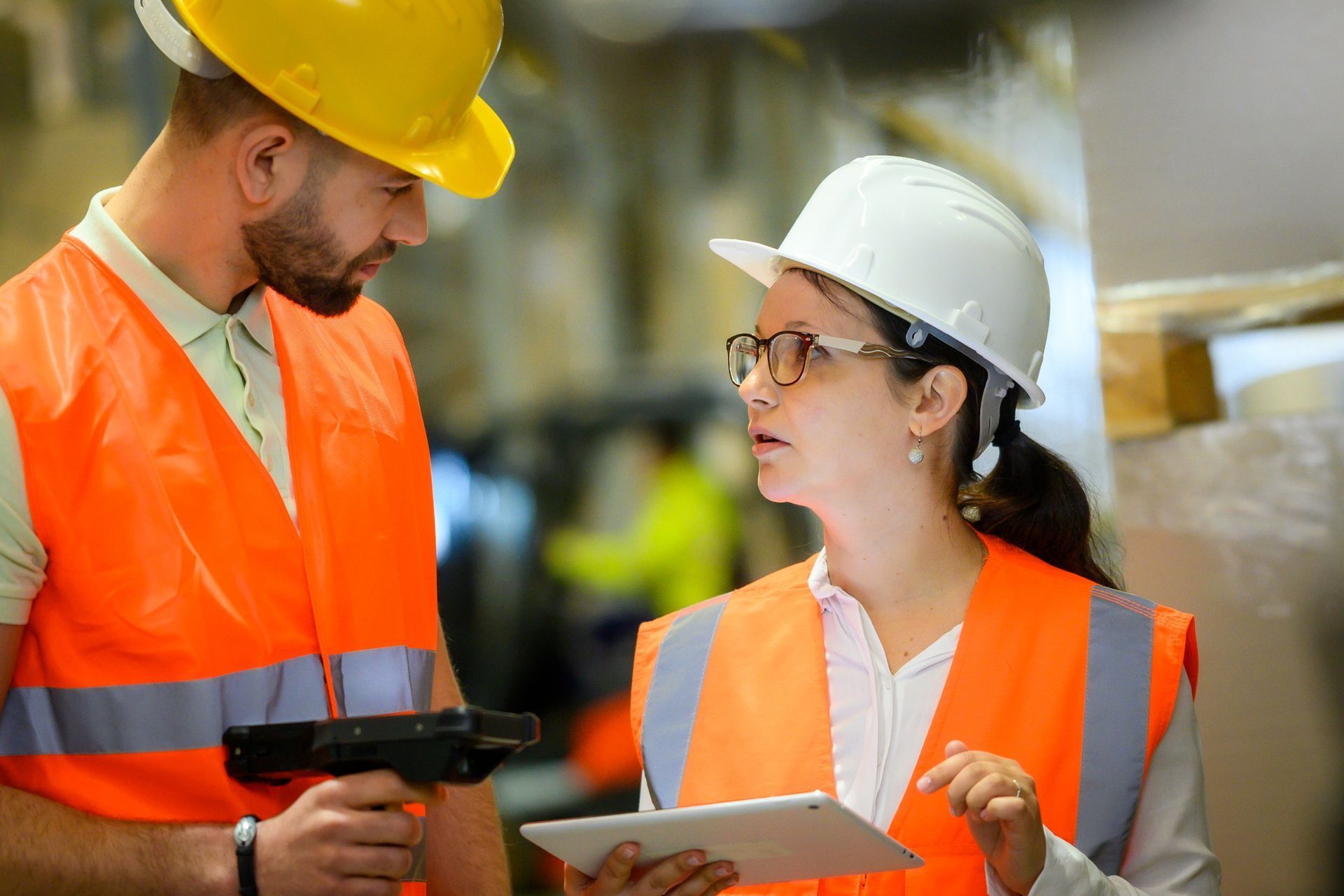Two workers in safety gear using tablet and scanner in warehouse.