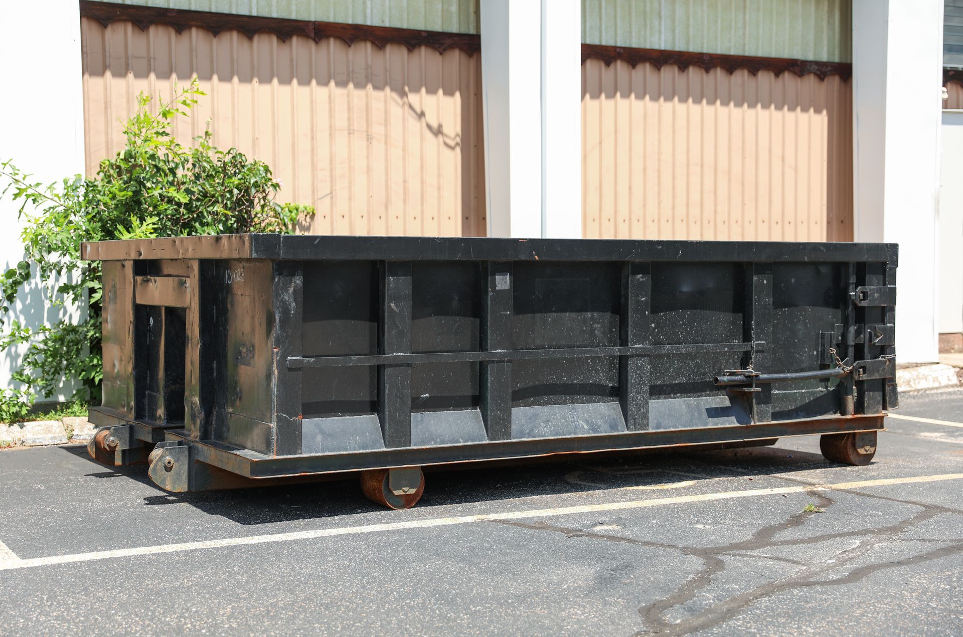 A large black dumpster is parked in a parking lot in front of a building.