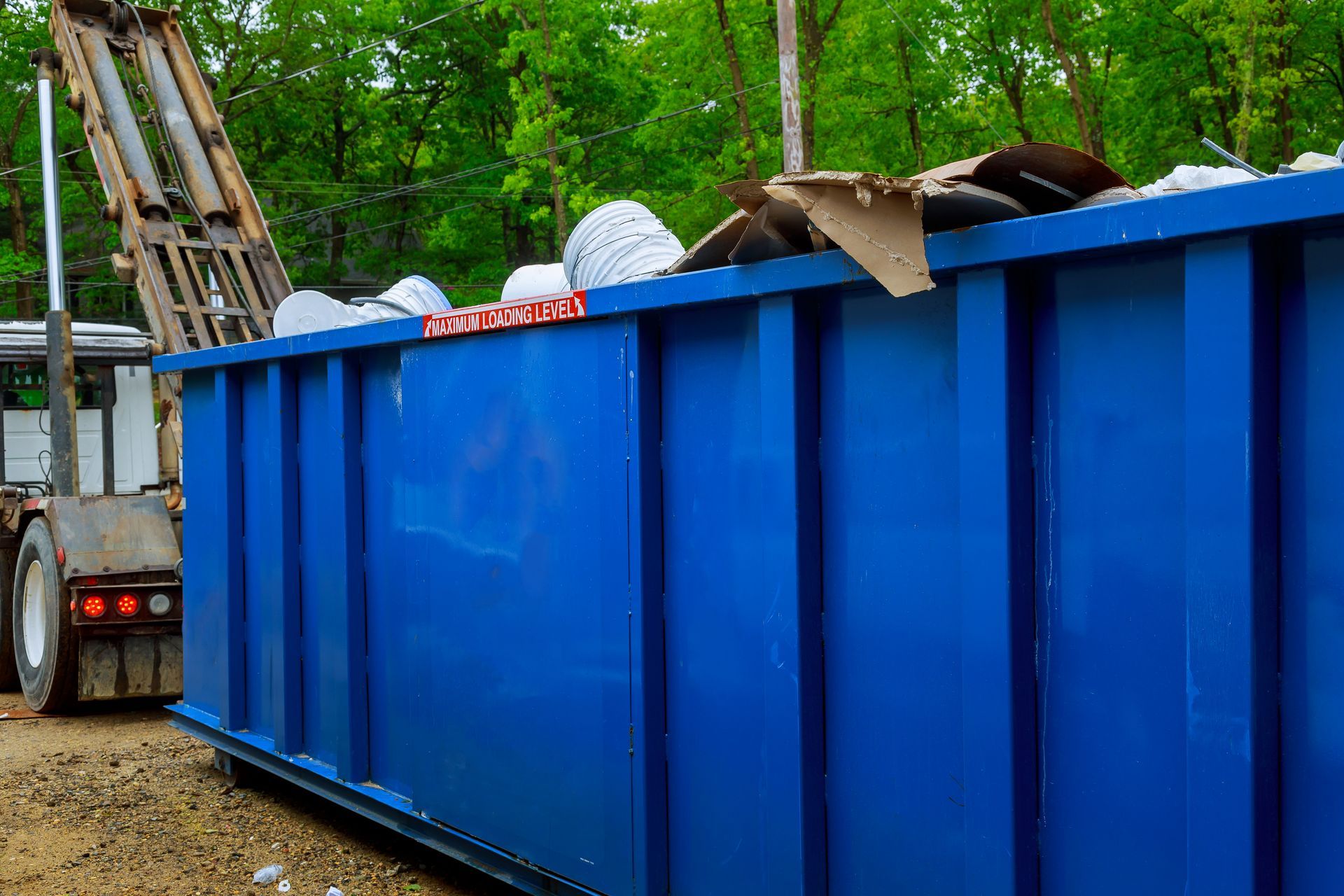 A blue dumpster filled with garbage is sitting next to a truck.