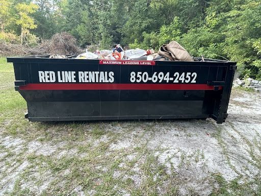 Black Red Line Rentals dumpster filled with debris in an outdoor setting. Phone number 850-694-2452.