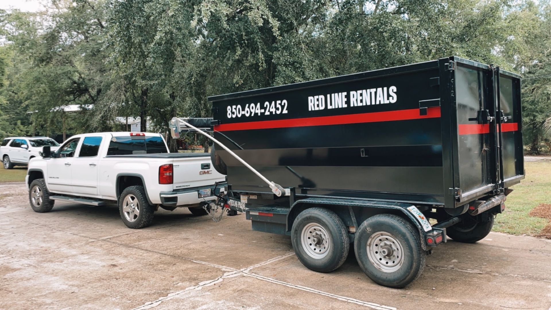 A white truck is towing a dumpster on a trailer.