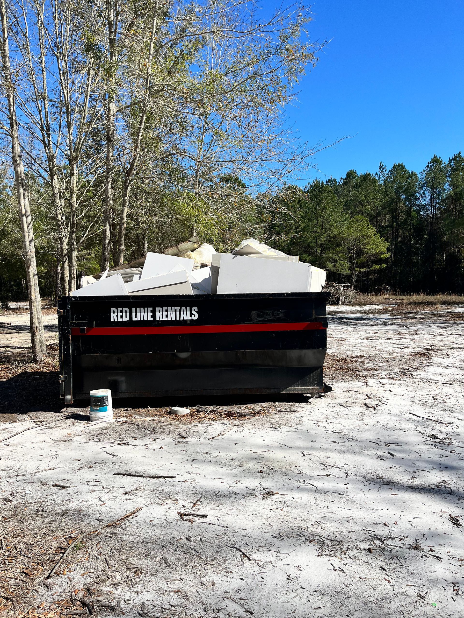 A dumpster is sitting in the middle of a dirt field.
