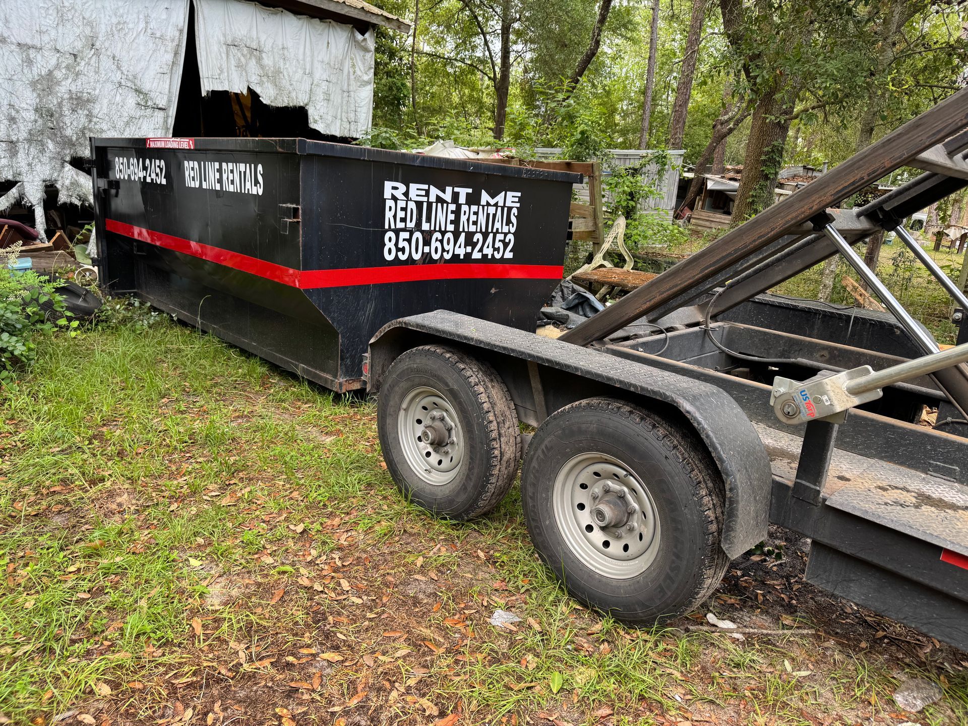 A dumpster is sitting on top of a trailer in the grass.