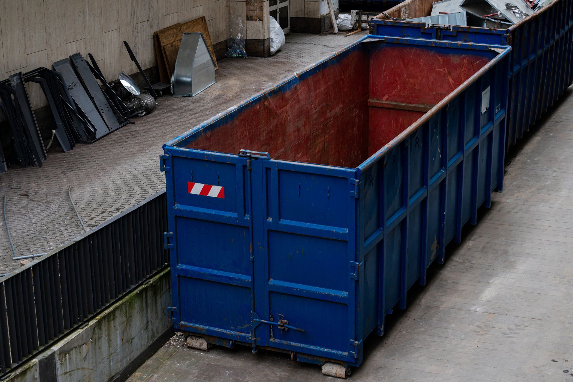 A blue dumpster is sitting on the ground next to a wall.