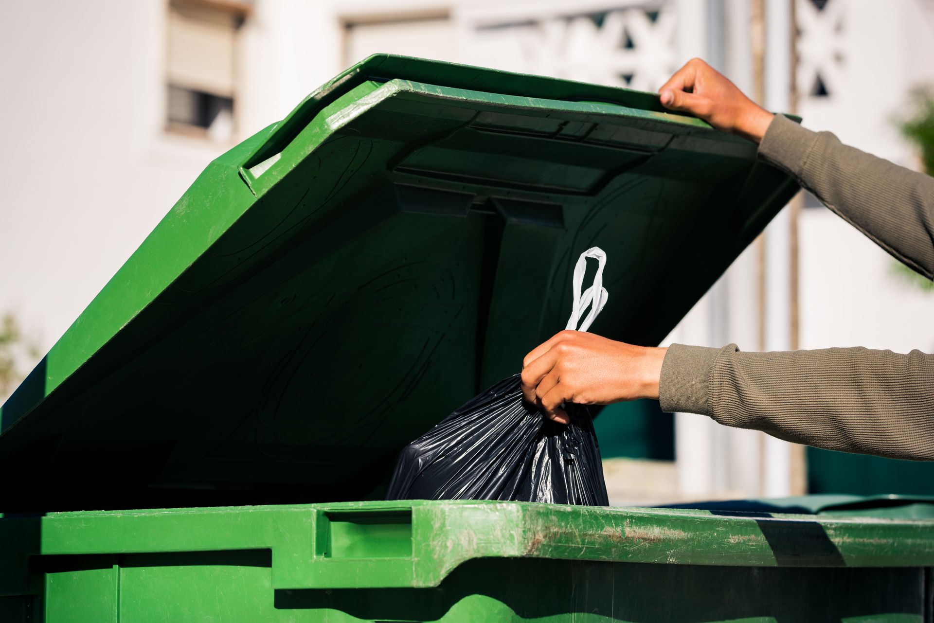A person is putting a black trash bag into a green trash can.
