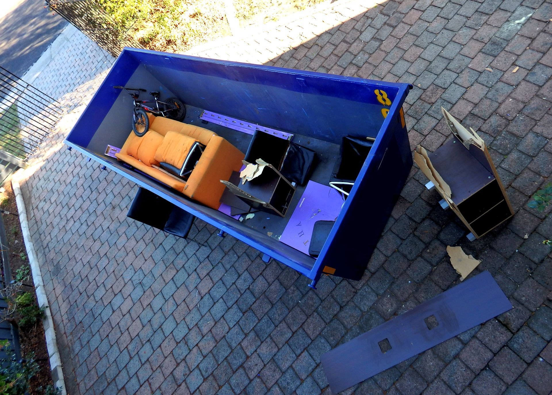 A blue dumpster filled with furniture and a bicycle