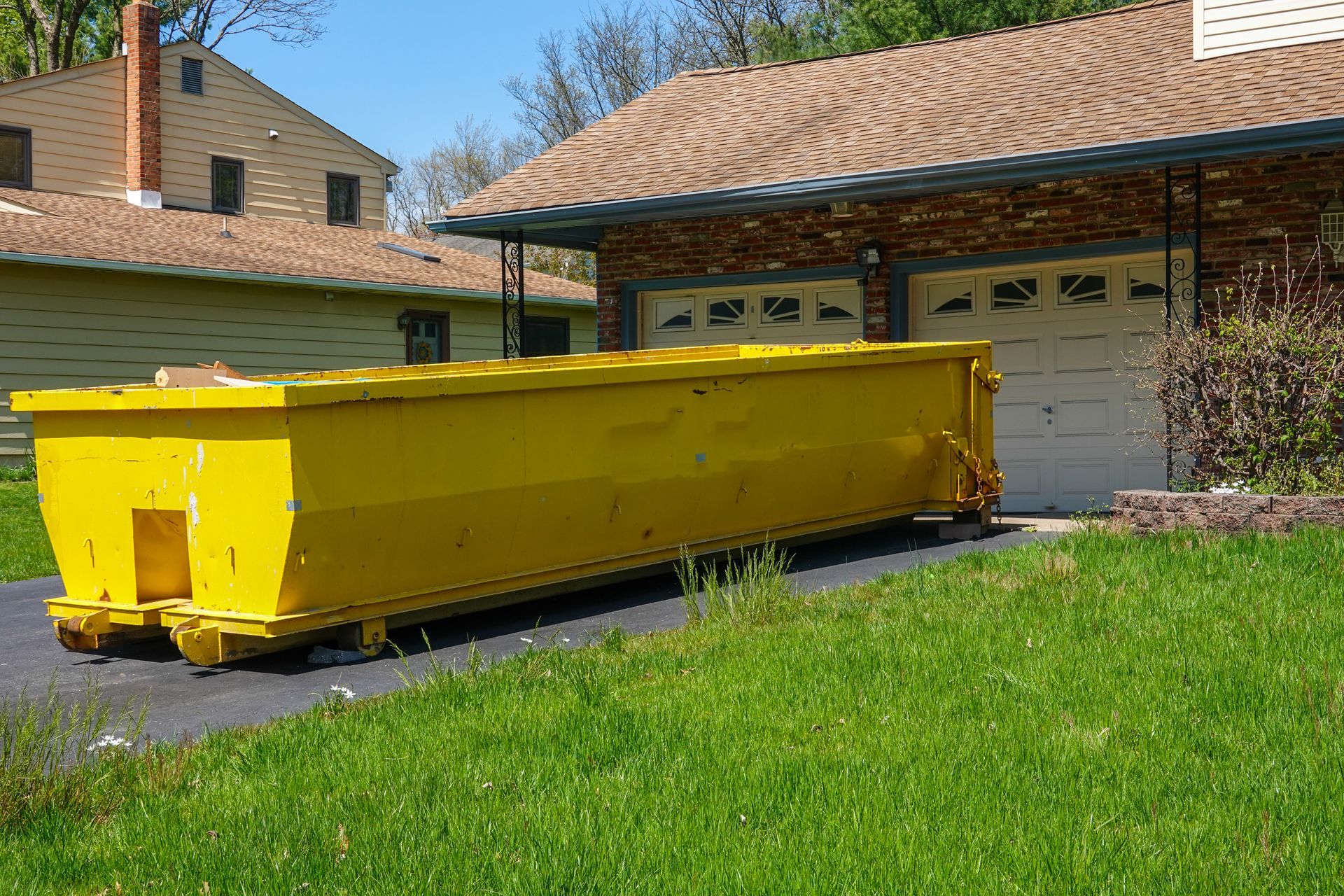 A large yellow dumpster is parked in front of a house.
