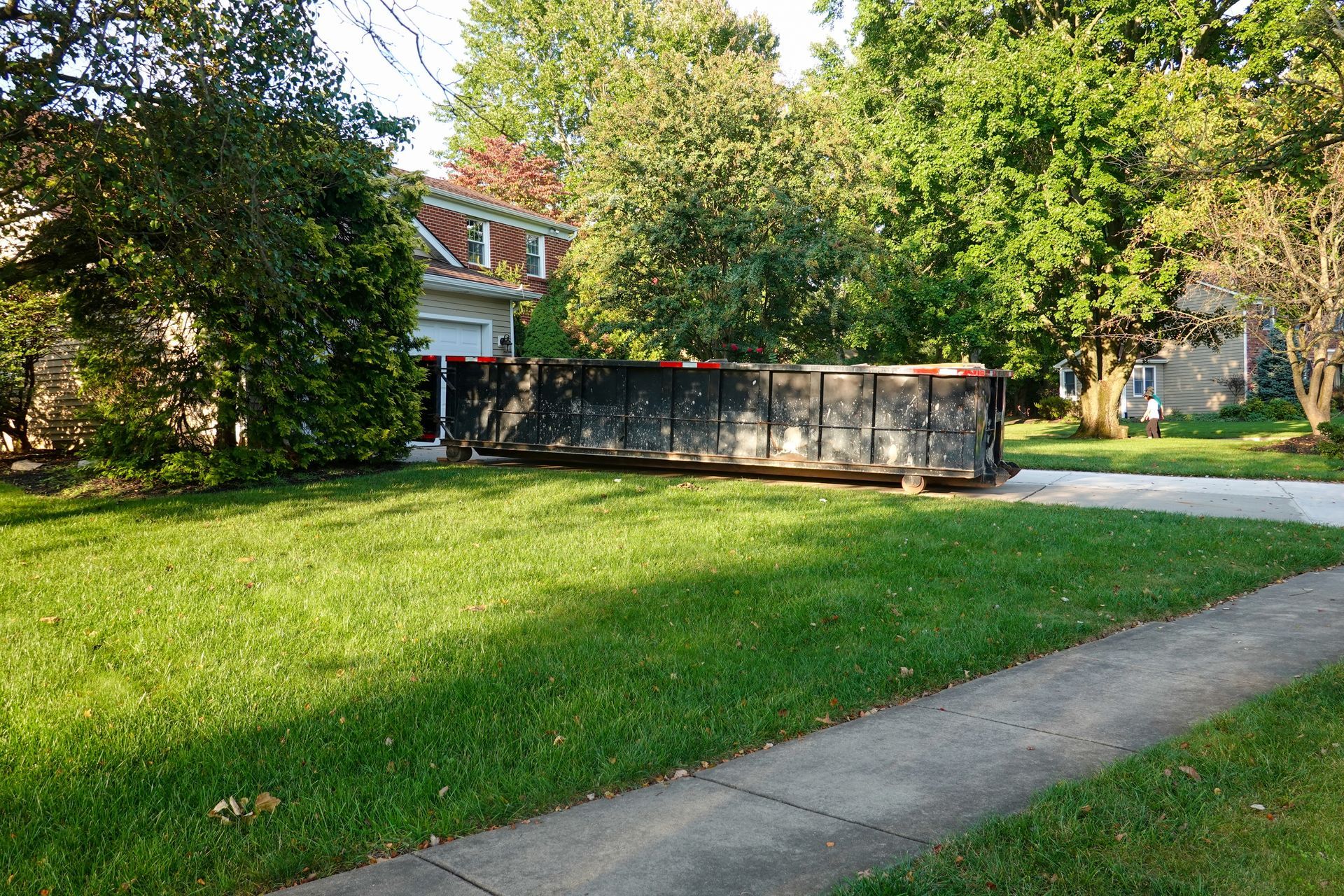 A dumpster is parked in the grass in front of a house.