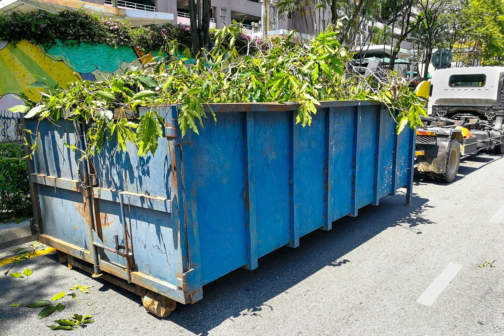 A blue dumpster filled with leaves is parked on the side of the road.